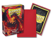 The image showcases a Dragon Shield: Japanese Size 60ct Sleeves - Ruby (Matte) box from Arcane Tinmen, featuring artwork of a red dragon on the cover. The text "Japanese Size Ruby - 60 Matte Sleeves" is clearly visible. Beside the box, there's a red card sleeve, and behind it is a card with the Dragon Shield logo on a black, textured background—making these ideal TCG sleeves for collectors.