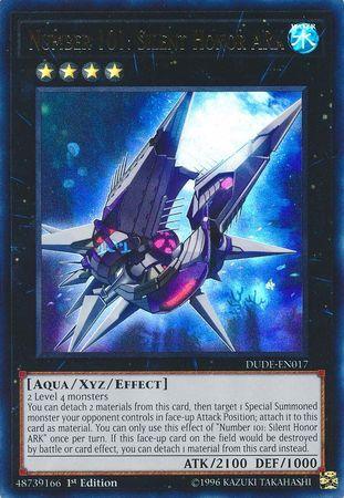 The image shows a Yu-Gi-Oh! trading card titled "Number 101: Silent Honor ARK [DUDE-EN017] Ultra Rare," an Xyz/Effect Monster. It features an armored, futuristic spaceship with a sleek design and glowing lights. The card is labeled with various attributes and text detailing its abilities and stats, which include ATK/2100 and DEF/1000.