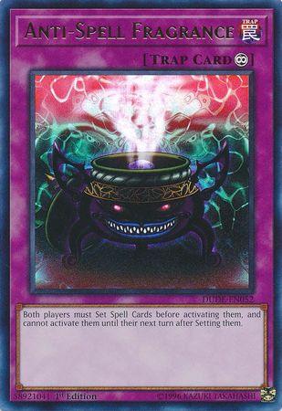 A Yu-Gi-Oh! Continuous Trap Card titled "Anti-Spell Fragrance [DUDE-EN052] Ultra Rare." The card, found in the Duel Devastator set, features a purple cauldron with glowing red eyes and an ominous grin. A swirling mist rises from the cauldron against a mystical pink and green haze. This Ultra Rare card restricts the activation of Spell Cards.