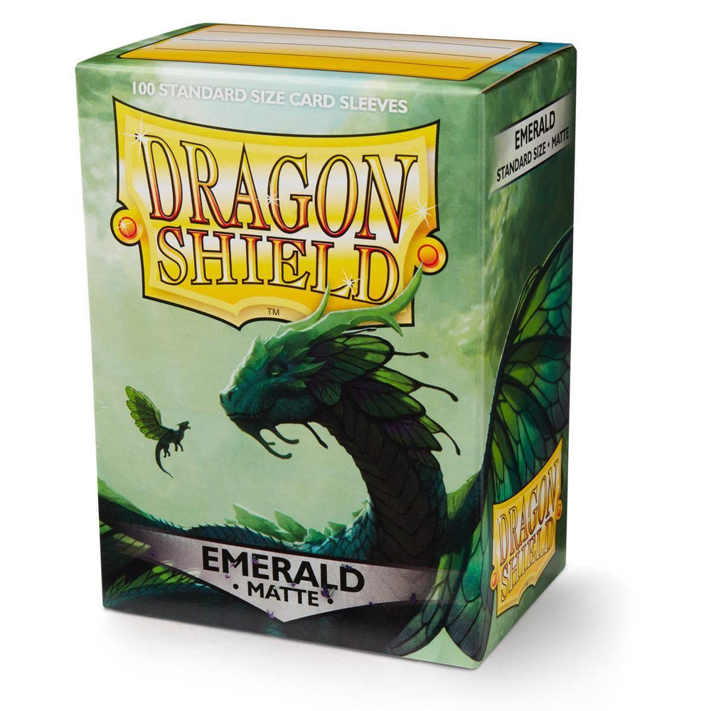 The image shows a box of Dragon Shield: Standard 100ct Sleeves - Emerald (Matte) by Arcane Tinmen, featuring green dragon artwork with large wings and intricate design on a light green background. A smaller green creature also appears, enhancing the fantasy theme of these matte sleeves.