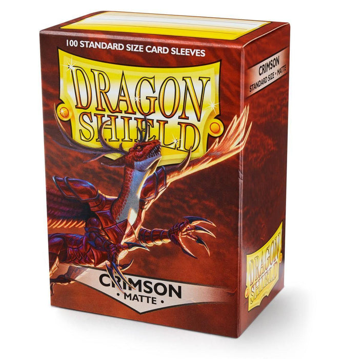 A colorful box of Dragon Shield: Standard 100ct Sleeves - Crimson (Matte) featuring a crimson matte finish. The box displays the iconic Arcane Tinmen logo with a stylized red dragon extending its wings and claws. The package indicates it contains 100 standard-size matte sleeves, perfect for avid collectors and players alike.