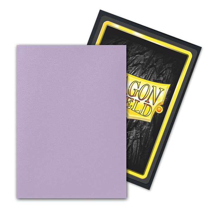 A soft Dragon Shield: Standard 100ct Sleeves - Orchid (Dual Matte) by Arcane Tinmen is placed overlapping a card featuring a "Dragon Shield" design. The Dragon Shield card has a black textured background with a yellow and black border, and the "Dragon Shield" logo is prominently displayed at the center.