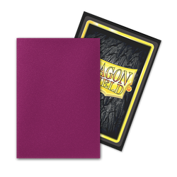 In the foreground, a card sleeve from the **Dragon Shield: Japanese Size 60ct Sleeves - Wraith (Dual Matte)** collection by **Arcane Tinmen** is showcased in a solid, magenta color. Behind it, a card emerges partially visible, presenting a textured black background encased in a yellow frame with the bold, stylized text "DRAGON." The arrangement strongly appeals to TCG enthusiasts seeking Dragon Shield sleeves.