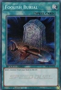 An image of the Foolish Burial (Secret) [SBCB-EN139] Secret Rare Spell Card from the Yu-Gi-Oh! trading card game. The Secret Rare artwork depicts a grave with a tombstone and a shovel stuck in the ground. The card text reads: "Send 1 monster from your Deck to the GY." The borders and text areas are light blue with a marbling effect.