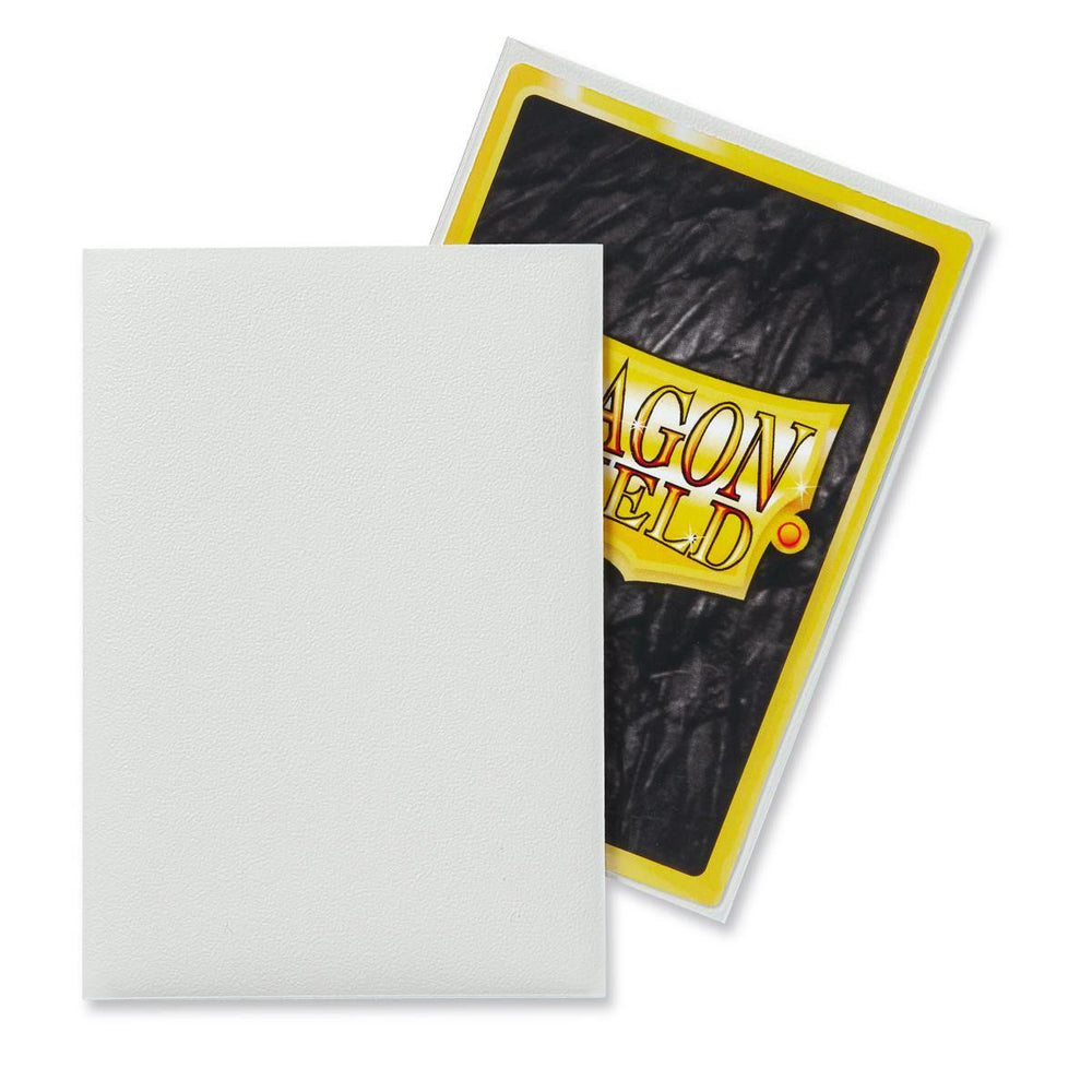 Two trading cards are shown; one faces forward and appears blank with a white surface, and the other faces backward revealing a stylized design. The second card has a yellow border with partial text "AGON FIELD" visible on a wrinkled black background. They are both slightly tilted in Dragon Shield: Japanese Size 60ct Sleeves - White (Matte) from Arcane Tinmen.