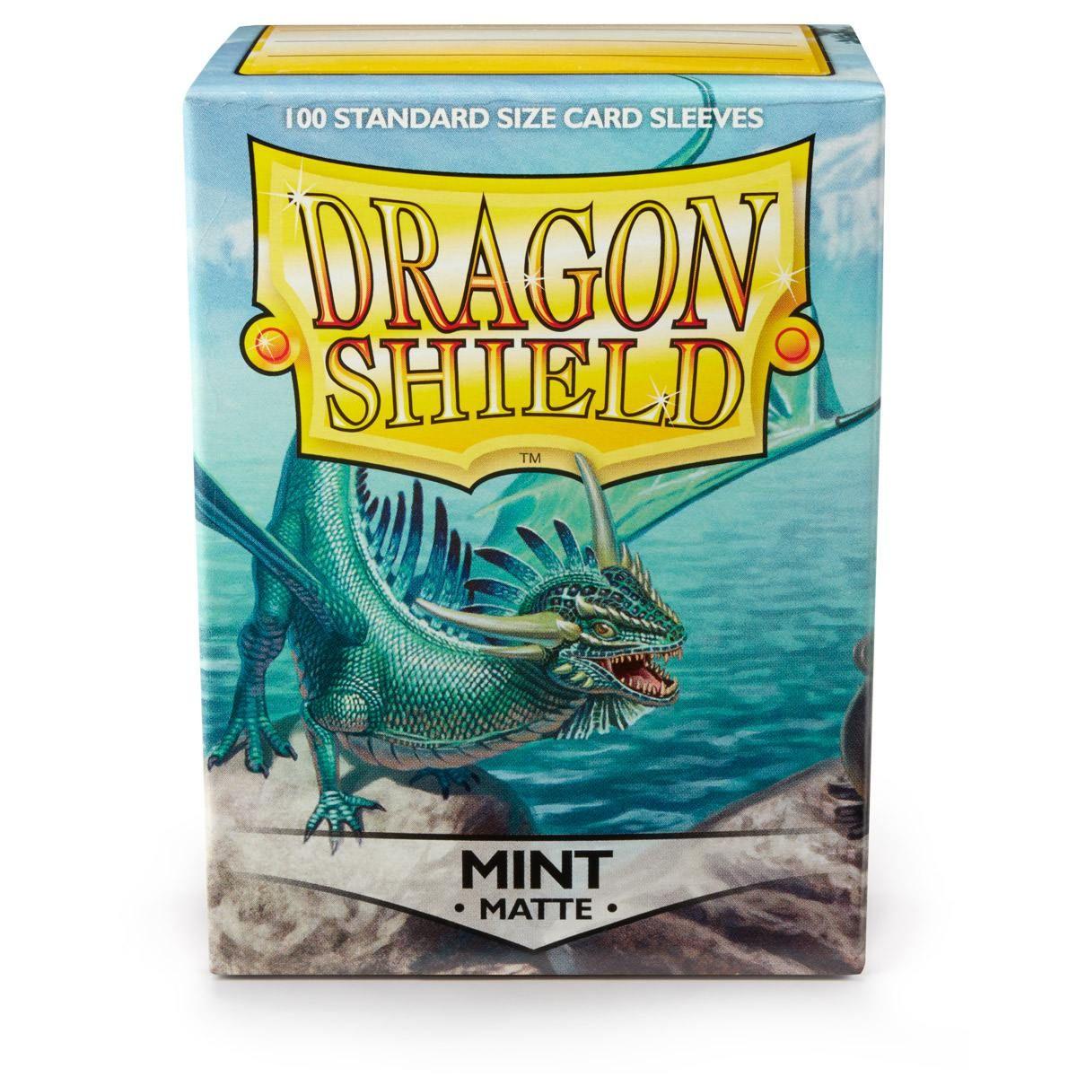 A box of Arcane Tinmen's Dragon Shield: Standard 100ct Sleeves - Mint (Matte) is displayed, featuring a vibrant green dragon near a shimmering lake with majestic mountains. Bold text announces 