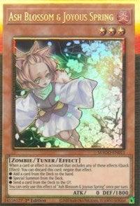 A Yu-Gi-Oh! trading card named "Ash Blossom & Joyous Spring [MAGO-EN011]" Gold Rare. The card showcases an anime-style young girl with brown hair, wearing a white kimono adorned with red and green trim, surrounded by vibrant, glowing particles. This Tuner/Effect Monster has 0 ATK and 1800 DEF.