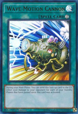 The image shows the Yu-Gi-Oh! trading card "Wave-Motion Cannon [DUDE-EN039] Ultra Rare," an Ultra Rare Continuous Spell Card. The artwork features a futuristic blue-green cannon with glowing energy and wires, firing a powerful beam. The card text describes its effect of inflicting 1000 damage for each Standby Phase passed.