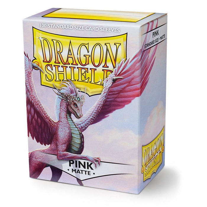 An image of a Dragon Shield: Standard 100ct Sleeves - Pink (Matte) box by Arcane Tinmen. The box features a fantasy-themed illustration of a pink dragon with wings extended, framed by a yellow and gold banner. The text reads, "Dragon Shield," with "Pink Matte" below. The top-left mentions "100 Standard Size Matte sleeves.