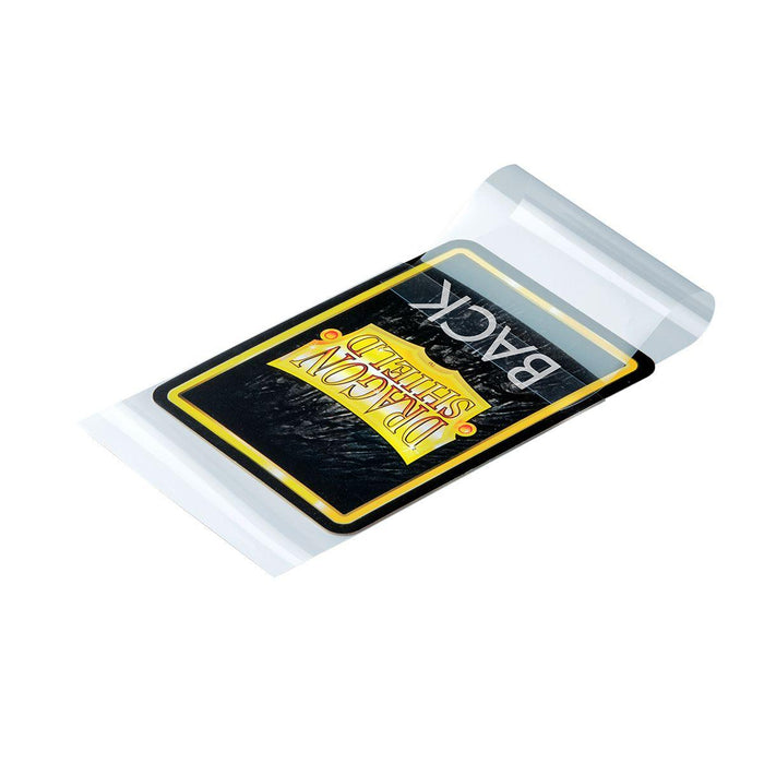 A deck of Arcane Tinmen Dragon Shield: Japanese Size 100ct Inner Sleeves - Perfect Fit (Sealable / Clear 'Yama'), perfectly sized with Japanese Size Sleeves, is partially enclosed in a transparent plastic packaging. The visible part of the topmost card sleeve proudly displays the Dragon Shield logo in gold with a sleek black background.