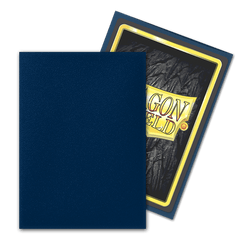 A blue card album cover partially hides a trading card in Arcane Tinmen's Dragon Shield: Standard 100ct Sleeves - Midnight Blue (Matte). The card has a dark textured background, yellow border, and bold "DRAGON SHIELD" text in yellow and red at the center.