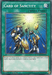 The image depicts the Yu-Gi-Oh! "Card of Sanctity [YGLD-ENC27] Common," a Normal Spell card featured in Yugi's Legendary Decks. The art shows three armored warriors reaching towards a glowing light above, with coins and golden items falling around them. The card has a green border, marked "SPELL CARD" with instructions below the artwork.